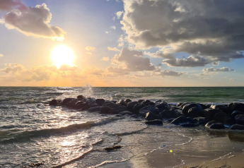 Coucher de soleil sur la mer, rochers et vagues près d'une maison de vacances à Melby, Danemark.