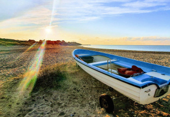 Petite barque sur une plage au coucher du soleil près du « 6 person holiday home in Melby », Danemark.