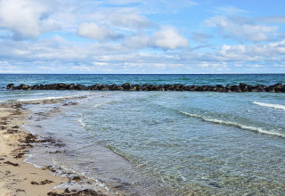 Acqua cristallina, spiaggia sabbiosa e barriera rocciosa vicino alla casa vacanza a Melby, Danimarca.