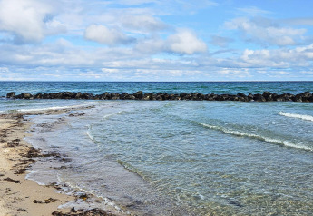Strand med klart vand, stenbrydning og blå himmel nær 6 personers feriehus i Melby, Danmark.