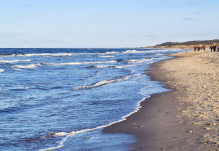 Photo de la plage à Melby, Danemark, près d'une maison de vacances, avec des vagues et des promeneurs.