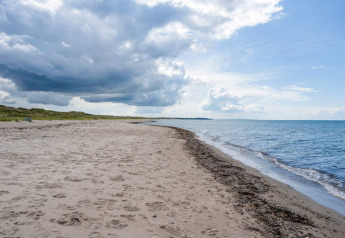 Zandstrand en zee bij een vakantiewoning voor 6 personen in Melby, Denemarken, met bewolkte lucht.