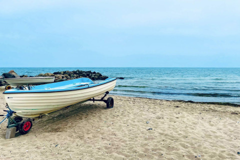 Un bateau sur la plage de Melby, Danemark, avec la mer calme et des rochers en arrière-plan.