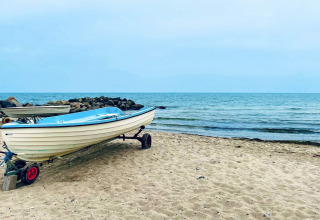 Ein Boot steht am Sandstrand in Melby, Dänemark, mit Steinen und ruhigem Meer im Hintergrund.
