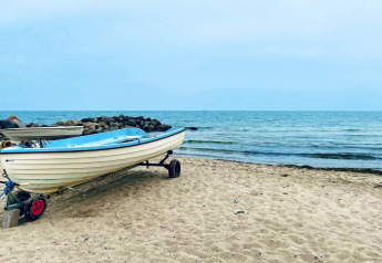 En båd står på stranden ved havet i Melby, Danmark, med klipper og blåt hav i baggrunden.