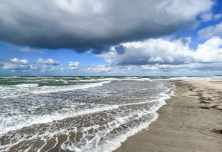 Golven spoelen aan op zandstrand onder wolken bij een 6-persoons vakantiehuis in Melby, Denemarken.