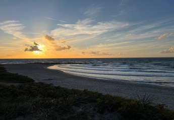 Atardecer en la playa visto desde una cabaña en Melby, Dinamarca, con olas suaves y cielo tranquilo.