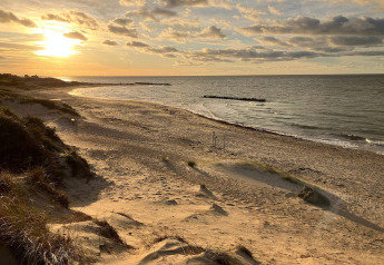 Solnedgang over en fredelig sandstrand ved Melby, Danmark, set fra klitterne tæt på ferieboligen.