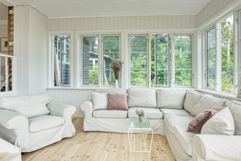 Séjour lumineux et confortable avec canapés blancs et grandes fenêtres dans maison de vacances à Melby, Danemark.