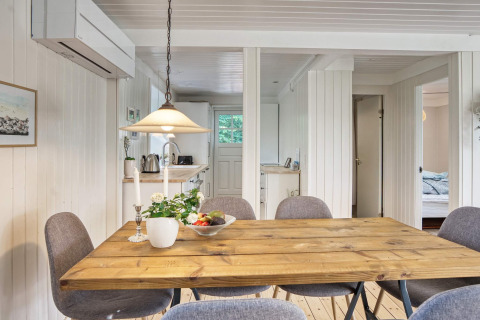 Spiseområde i feriehus i Melby, Danmark, med træbord, grå stole, blomster og frugtskål på bordet.