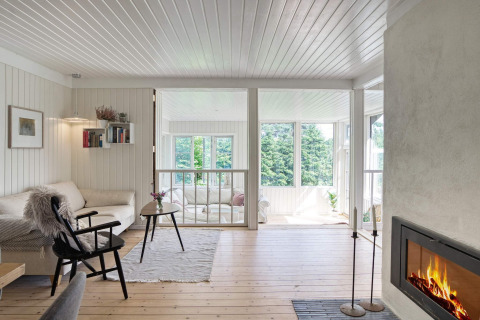 Stue med moderne pejse, lyse vægge og loft, store vinduer med udsigt til grøn natur i Melby, Danmark.