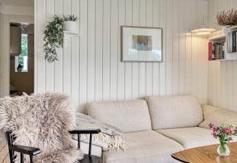 Cozy living room in Melby holiday home, Denmark, featuring a comfy sofa, bookshelves, plants, and artwork.
