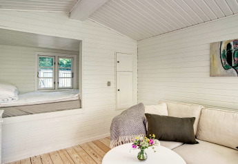 Intérieur lumineux d’une maison de vacances à Melby, Danemark, avec canapé, table et coin nuit douillet.