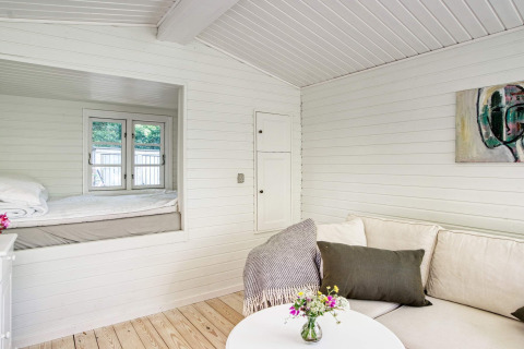 Licht interieur van vakantiehuis in Melby, Denemarken, met sofa, salontafel en knusse slaaphoek.