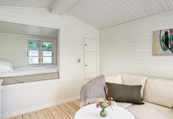 Licht interieur van vakantiehuis in Melby, Denemarken, met sofa, salontafel en knusse slaaphoek.