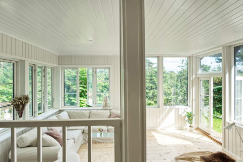 Lyst opholdsområde i sommerhus i Melby, Danmark, med store vinduer og udsigt til grøn natur.