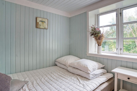 Lyst og hyggeligt soveværelse med pastelfarvede vægge, vindue, dobbeltseng og blomster på vindueskarmen.