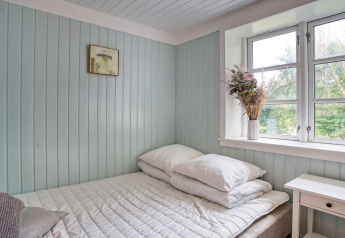 Lyst og hyggeligt soveværelse med pastelfarvede vægge, vindue, dobbeltseng og blomster på vindueskarmen.