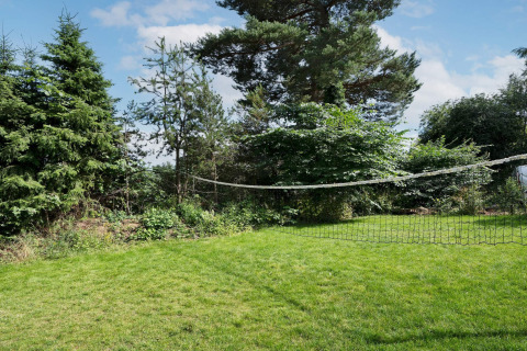 Groene tuin met badmintonnet bij 6-persoons vakantiehuis in Melby, Denemarken, tussen de bomen.