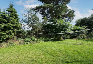 Groene tuin met badmintonnet bij 6-persoons vakantiehuis in Melby, Denemarken, tussen de bomen.