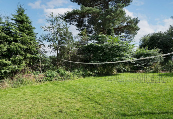 Groene tuin met badmintonnet bij 6-persoons vakantiehuis in Melby, Denemarken, tussen de bomen.