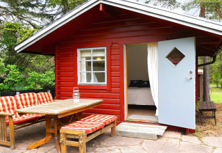 Rood houten chalet met open blauwe deur en tuinmeubels bij '6-persoons vakantiehuis in Mönsterås', Zweden.