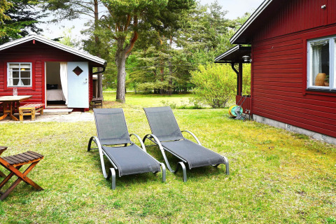 Zwei Sonnenliegen auf einer Wiese vor roten Holzhäusern bei der 6-Personen-Ferienwohnung in Mönsterås, Schweden.