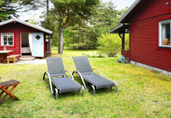 To liggestole og et sommerhus med rød facade i en grøn have ved 6 personers feriebolig i Mönsterås, Sverige.