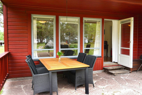 Udendørs terrasse med træbord og fire stole ved en rød hytte, feriehus til seks i Mönsterås, Sverige.