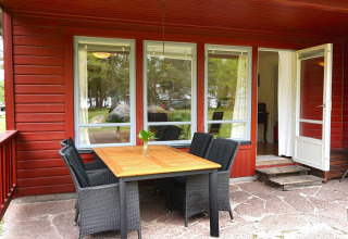 Terrasse extérieure avec table et chaises devant un chalet rouge pour six à Mönsterås en Suède.