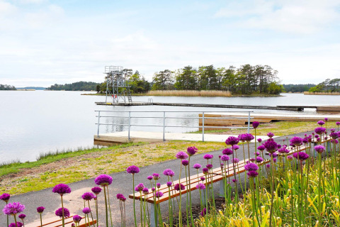 Uitzicht op meer met duikplatform, houten steigers en paarse bloemen bij vakantiewoning in Mönsterås, Zweden.