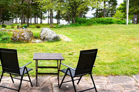Deux chaises de jardin noires et une petite table sur une terrasse avec pelouse et arbres à Mönsterås, Suède.