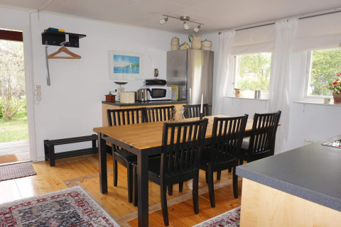 Sala da pranzo con sei sedie nere, tavolo in legno e cucina luminosa in una casa vacanza a Mönsterås, Svezia.