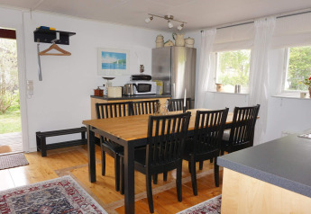 Salle à manger avec six chaises noires, table en bois, et cuisine lumineuse dans une maison à Mönsterås, Suède.