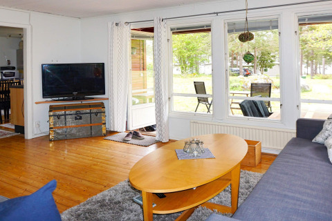 Sala luminosa en lodge en Mönsterås, Suecia, con sofá, televisor, mesa de centro y grandes ventanales.