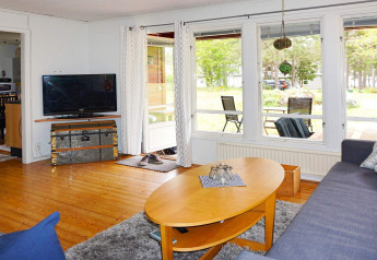 Lyst opholdsområde i lodge med træbord, sofa, TV og store vinduer mod veranda i Mönsterås, Sverige.