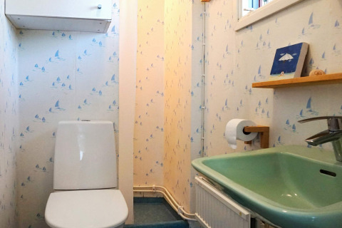 Bagno luminoso con WC, lavandino verde e carta da parati a barche a vela in una casa vacanze a Mönsterås, Svezia.