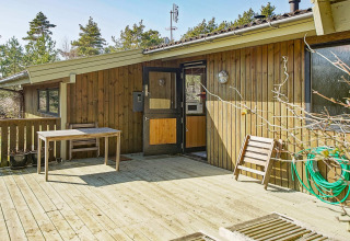 Houten terras met tafel en stoel bij Seaside Serenity lodge in Snogebaek, Denemarken, omringd door bomen.