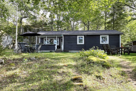 Zwart vakantiehuis voor 6 personen in Rimforsa, Zweden, omgeven door bomen en gras, met tuinmeubilair