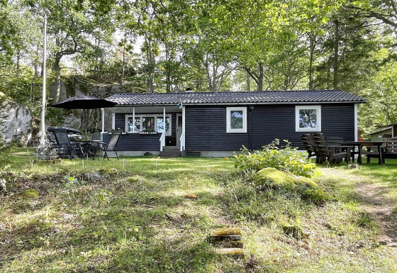 Zwart vakantiehuis voor 6 personen in Rimforsa, Zweden, omgeven door bomen en gras, met tuinmeubilair