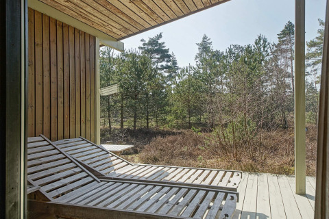 Zonneterras met houten ligstoelen bij Seaside Serenity in Snogebaek, Denemarken, zicht op het bos.