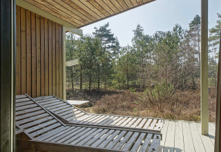 Zonneterras met houten ligstoelen bij Seaside Serenity in Snogebaek, Denemarken, zicht op het bos.