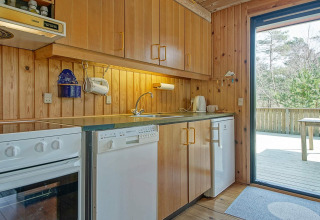 Cocina revestida de madera en Seaside Serenity en Snogebaek, Dinamarca, con electrodomésticos modernos y terraza.