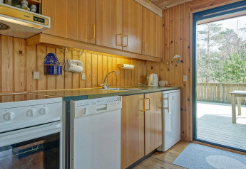 Keuken met houten lambrisering bij Seaside Serenity in Snogebaek, Denemarken, met apparaten en zicht op terras.