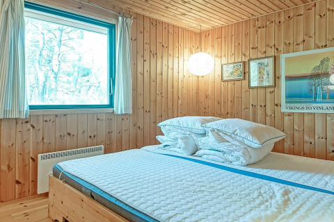 Chambre douillette en bois avec grand lit, fenêtre et tableaux muraux à Seaside Serenity à Snogebaek, Danemark.