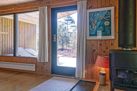 Interior de una cabaña con paredes de madera, chimenea, cuadro y vista a la naturaleza en Snogebaek, Dinamarca.