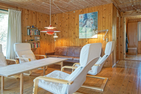 Sala de 'Seaside Serenity in Snogebaek' en Dinamarca con paredes de madera, sofá y sillas modernas.