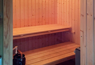 Vue intérieure du sauna en bois à Seaside Serenity à Snogebaek, Danemark, avec bancs et poêle à sauna.