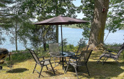 Udendørs spiseområde med fire stole, parasol og udsigt over en sø, omgivet af skov i Rimforsa, Sverige.