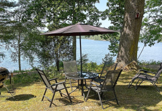 Buitentafel met stoelen en parasol aan een meer bij een vakantiehuis in Rimforsa, Zweden.